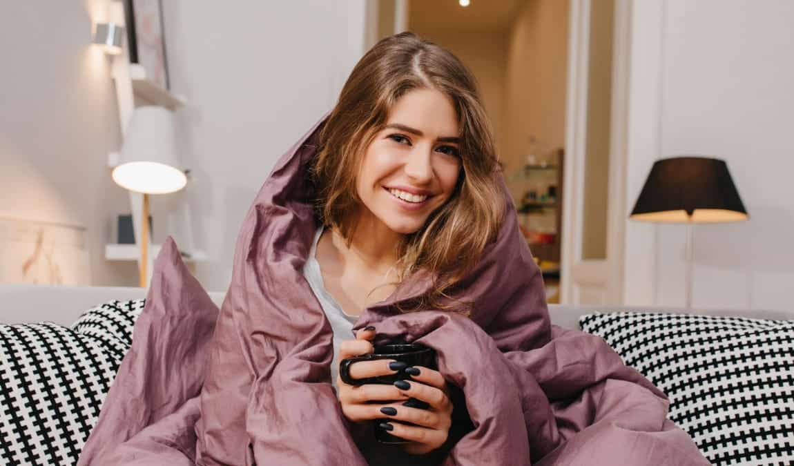 Photo d'une femme sur sont canapé se réchauffant avec un plaid et une tasse chaude